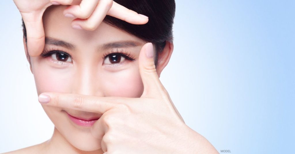 Asian woman (model) framing her eyes with her fingers.