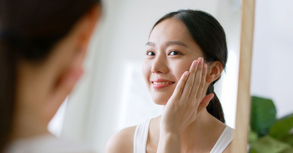 woman looking in mirror admiring her smile after Masseter BOTOX (MODEL)