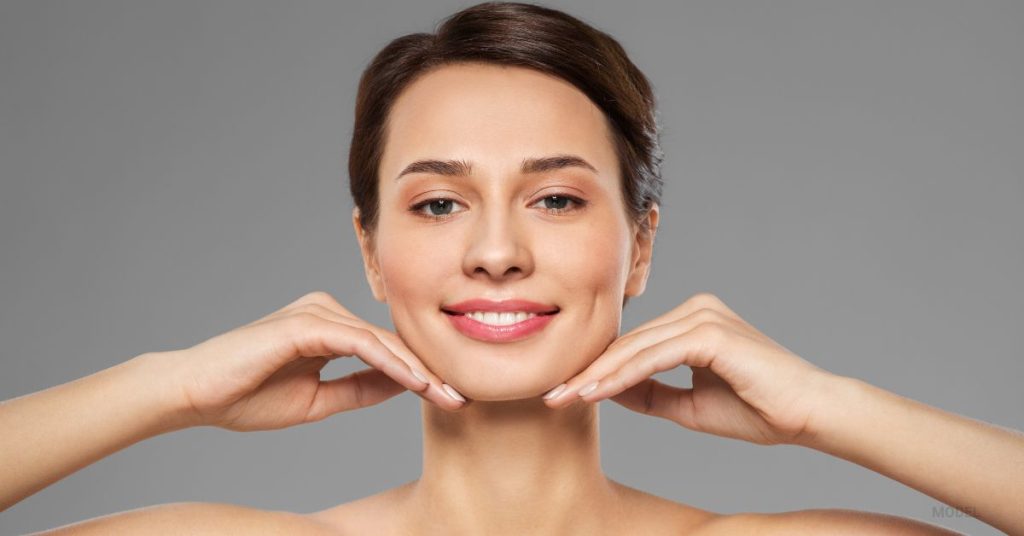 Women smiling with her hands palms side down touching her chin (MODEL)